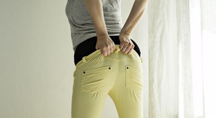 Woman standing in bedroom pulling on jeans, rear view